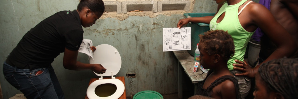 SOIL_Hygiene_Promoter Algate Joseph trains family EkoLakay toilet Photo credit Vic Hinterlang - copie